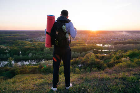 Young tourist guy with a backpack on top of a hill looking at the horizon and landscape in the...