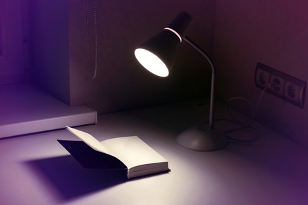 Lamp in socket and open book with a blank page for writing on white table in the evening or at night, toned in blue.の写真素材