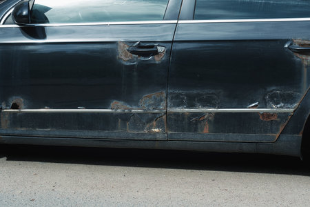 Rust and hard corrosion with small holes on black car body and doors on urban roadの写真素材