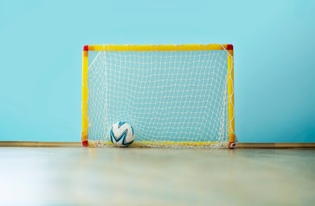 Football ball into soccer net of plastic children goal standing on wooden floor on playground insideの写真素材