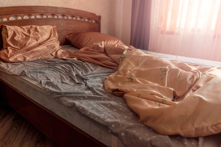 Single bed with a blanket and unmade bedclothes in bedroom of home or hotel room in early morningの写真素材