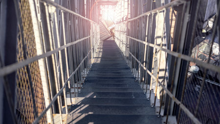 Abandoned staircase surrounded by steel mesh fence leading up to steel bridge with metal railings...