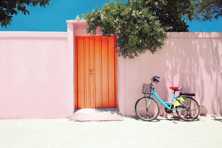 blue bike near pink facade wall with orange door under blue skyの写真素材