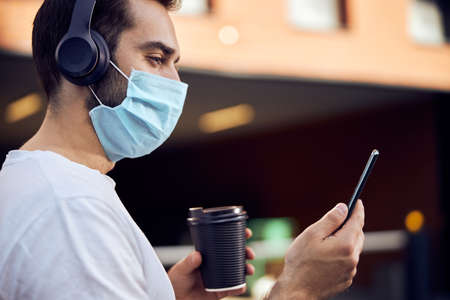 Masked man with coffee looking into the smartphone