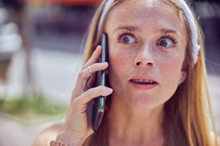 Red-haired pretty girl with braces is talking on the smartphone while looking away