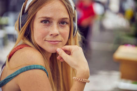Pretty red-haired girl is looking straight at camera while is touching her chin close up