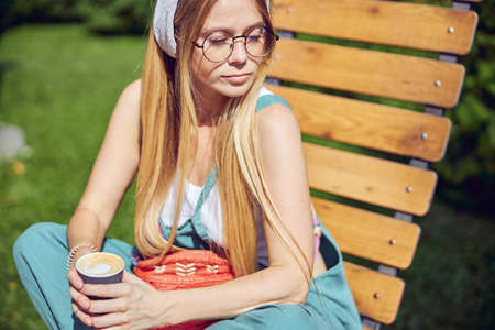 Pretty red-haired girl is holding a cup of coffee while is enjoying nature close up