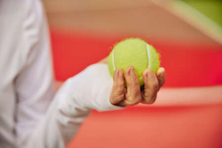 Old, healthy and cheerful lady on a colorfull square outdoors holding tennis ballの写真素材