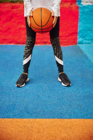 Old, healthy and cheerful lady with basketball ball on a colorfull square outdoors