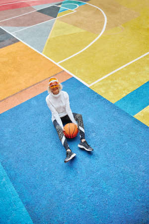 Old, healthy and cheerful lady with basketball ball on a colorfull square outdoorsの写真素材