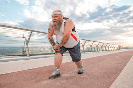 Fat caucasian bearded and bold man is doing morning exercses to loose his weight