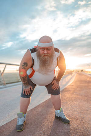 Fat caucasian bearded and bold man is doing morning exercses to loose his weight