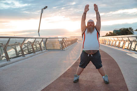 Fat caucasian bearded and bold man is doing morning exercses to loose his weight