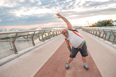 Fat caucasian bearded and bold man is doing morning exercses to loose his weightの写真素材