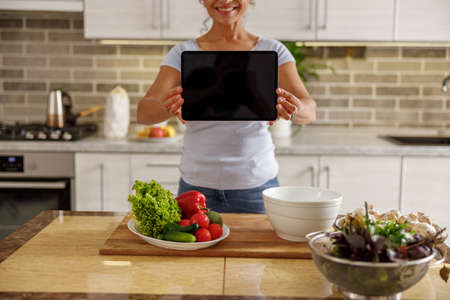 Beautiful smily handsome woman is preparing tasty fresh healthy salad at her kitchen at homeの写真素材