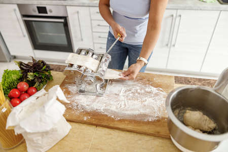 Beautiful smily handsome woman is preparing tasty fresh raw italian pasta at her kitchen at homeの写真素材