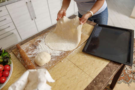 Beautiful smily handsome woman is preparing tasty fresh italian pizzawith vegetables at her kitchen...
