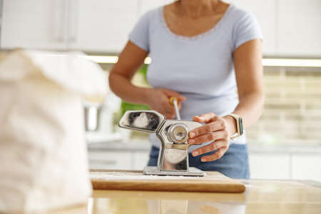 Beautiful smily handsome woman is preparing tasty fresh raw italian pasta at her kitchen at homeの写真素材