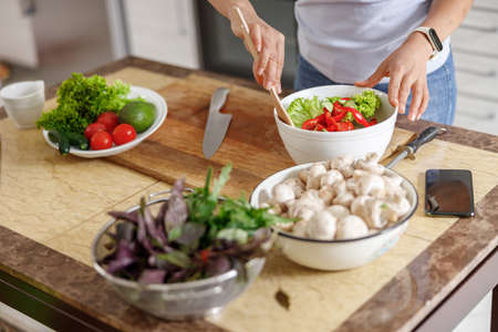 Beautiful smily handsome woman is preparing tasty fresh healthy salad at her kitchen at homeの写真素材