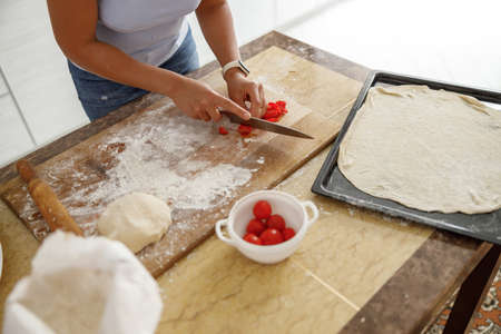 Beautiful smily handsome woman is preparing tasty fresh italian pizzawith vegetables at her kitchen at homeの写真素材