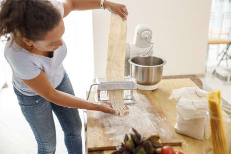 Beautiful smily handsome woman is preparing tasty fresh raw italian pasta at her kitchen at home