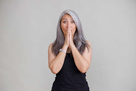 Emotional portraits of a paled long hair asian matured woman on gray background