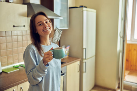 Young cheerful and happy woman is preparing tasty tea at her kitchen at homeの写真素材