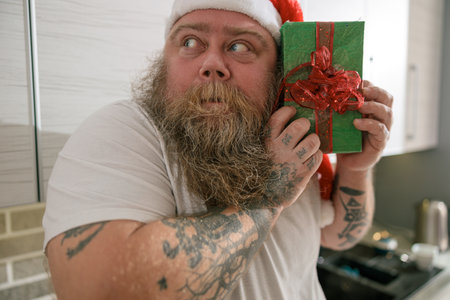 Emotional fat funny and tattooed man with present at the kitchen at homeの写真素材