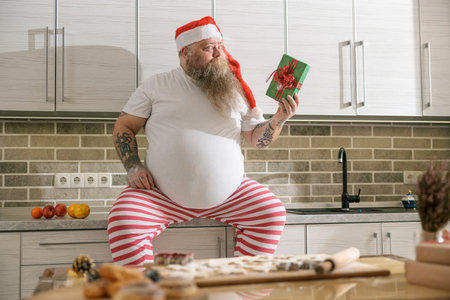 Emotional fat funny and tattooed man with present at the kitchen at homeの写真素材