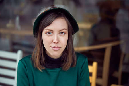 Happy woman in green dress in urban city is sitting near cafe
