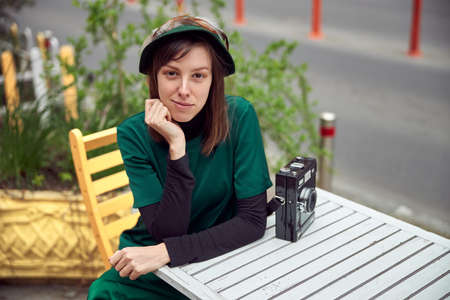 Happy woman in green dress in urban city is sitting near cafe