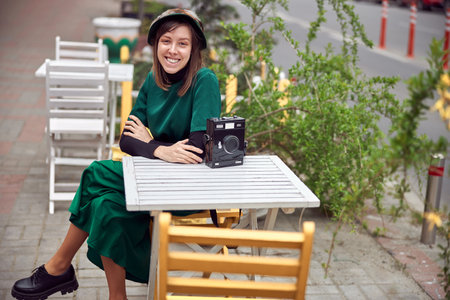 Happy woman in green dress in urban city is sitting near cafeの写真素材