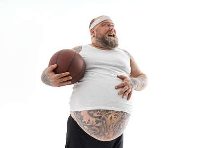 bearded fat caucasian tattoed man with basketball ball in white background. He is funny and happy