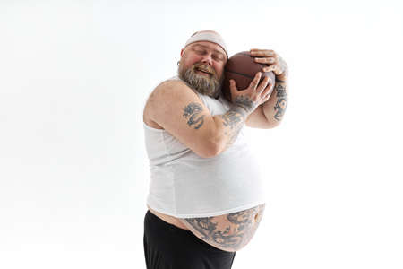 bearded fat caucasian tattoed man with basketball ball in white background. He is funny and happy