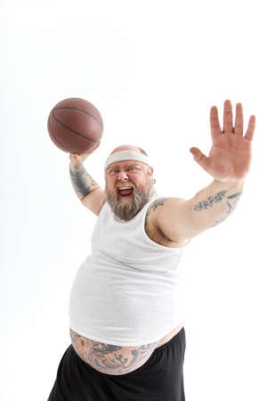 bearded fat caucasian tattoed man with basketball ball in white background. He is funny and happyの写真素材