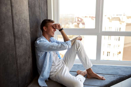 Happy adult caucasian male is sitting near panoramic window and chillingの写真素材