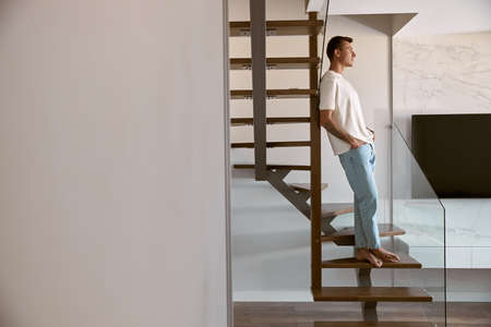 Relaxing happy caucasian man on the minimalistic stairs in modern light apartmentの写真素材