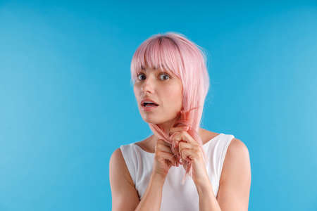 Portrait of surprised female model playing with pink hair, touching it while posing isolated over...