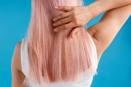 Close up shot of woman touching her smooth sleek natural long pink dyed hair while posing isolated over blue studio backgroundの写真素材