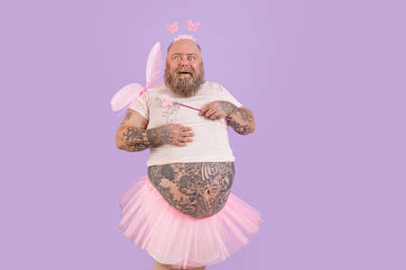 Bearded man with overweight in fairy suit with magic stick and wings on purple backgroundの写真素材