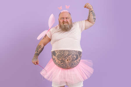 Brutal obese man with tattoos in fairy costume shows muscles on purple backgroundの写真素材