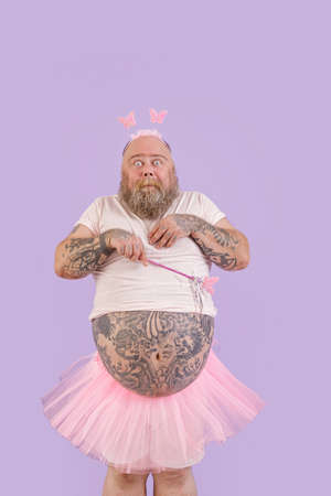 Shocked bearded man with overweight in fairy costume on purple backgroundの写真素材