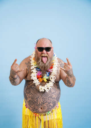 Funny man with overweight and flowers garland shows Horns gestures on light blue backgroundの写真素材