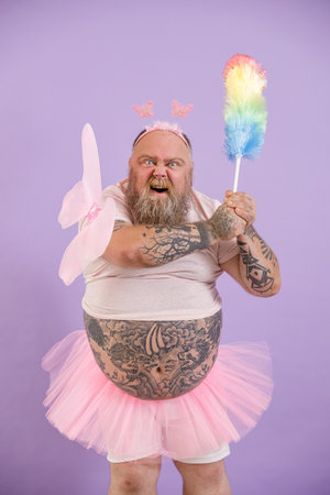 Bellicose obese person in fairy suit attacks with dust brush on purple backgroundの写真素材