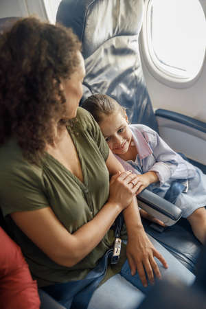 High angle view of little girl sitting on the plane, leaning on her mother while traveling togetherの写真素材
