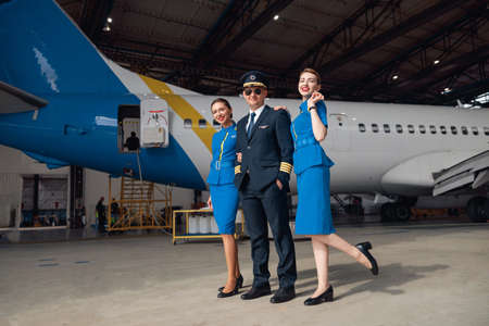 Full length shot of pilot in uniform and aviator sunglasses standing together with two air...