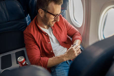 Handsome caucasian man in casual wear and glasses checking arrival time on his watch, sitting on the...