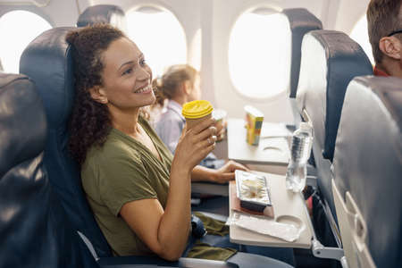 Happy female passenger drinking coffee and smiling while female flight attendant serving lunch on boardの写真素材