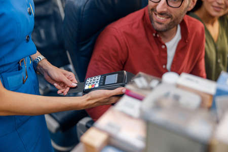 Close up shot of airline stewardess holding terminal while cheerful male passenger making paymentの写真素材