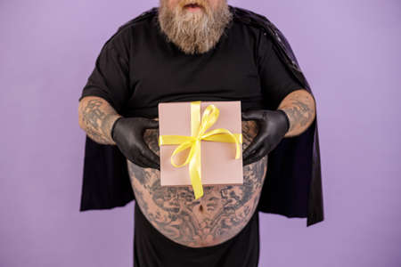 Plus size man on purple background closeup, focus on hands with gift boxの写真素材